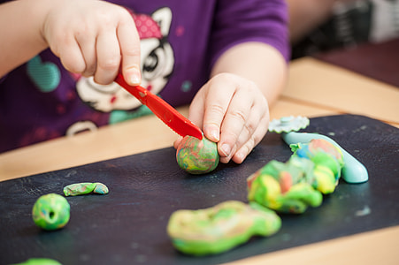 person holding red plastic knife on green toy clay thumbnail