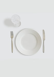 round white ceramic plate beside butter knife and fork with clear footed glass thumbnail