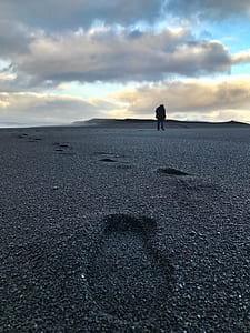 man walking on gray soil leaving footprints under cloudy sky during daytime thumbnail