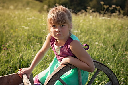 girl in maroon and teal sleeveless dress holding wagon wheel near green grass thumbnail