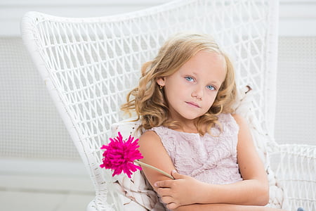 girl wearing pink floral top holding pink flower sitting on white chair thumbnail
