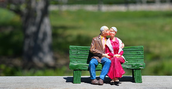 shallow focus photography of man wearing brown formal suit jacket and woman wearing red long-sleeved dress sitting on green bench ceramic figurine thumbnail