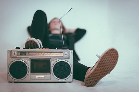 person leaning on white wall while near gray boombox thumbnail