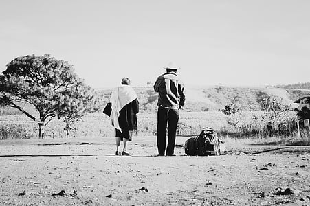 grayscale photo of man and woman standing near tree thumbnail