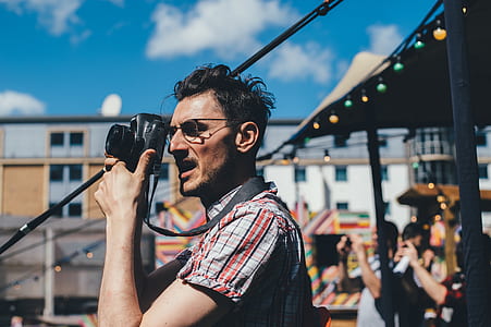 selective focus photo of man wearing eyeglasses taking a photo using black camera during daytime thumbnail
