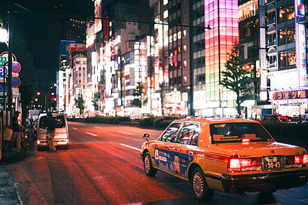 yellow sedan running on road near concrete buildings at night thumbnail