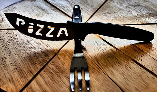 black pizza knife above fork on brown pizza board thumbnail