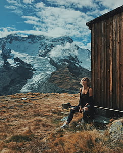 woman wearing black tank top and distressed black denim jeans while sitting near shed overlooking glacier mountain thumbnail
