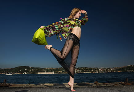 woman in black dress doing exercise near body of water during daytime thumbnail