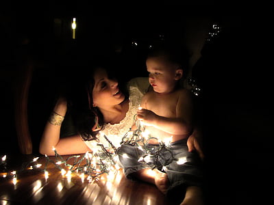 photo of woman laying on brown wooden floor with topless baby holding stringed lights thumbnail