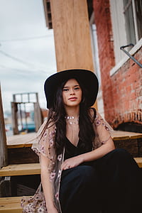 woman wearing black hat sitting on brown wooden stair during daytime shallow focus photography thumbnail
