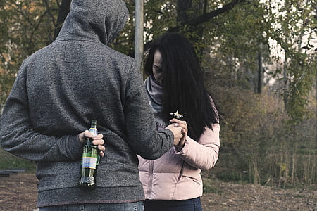 woman holding bottle on his back while giving flower to woman thumbnail