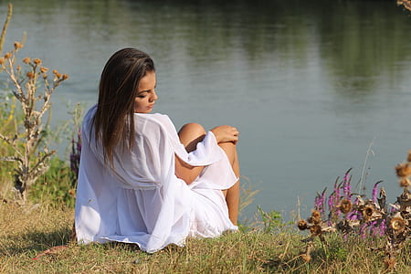 photo of woman sitting on grass in front of body of water thumbnail