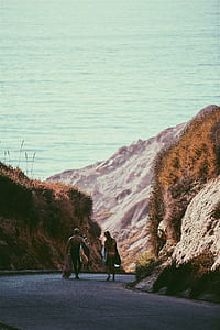 man and woman walking on road towards body of water thumbnail