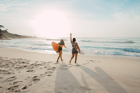 two woman walking on seashore with surfboard on hands thumbnail
