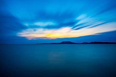 silhouette of mountain near sea under blue and yellow sky during golden hour thumbnail
