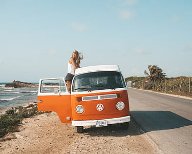 woman in white tank top standing in orange and white Volkswagen bus near the road thumbnail