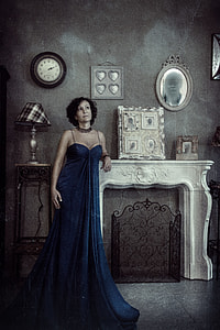 photo of woman in blue dress leaning on white concrete fireplace mantel staring above thumbnail