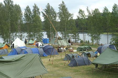 assorted-color tents on grass field near trees and calm water at daytime thumbnail
