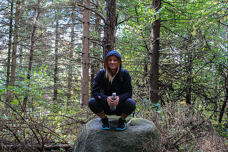 woman wearing hoodie sitting on rock formation surrounded by trees thumbnail