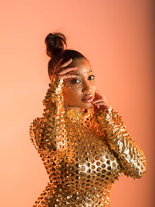 woman in gold long-sleeved tops holding her face standing near wall thumbnail