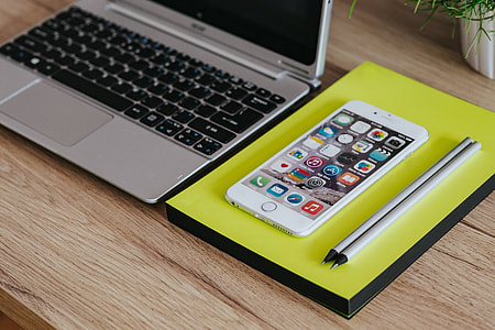 Silver Acer laptop, a white Apple iPhone and a notepad on a wooden desk thumbnail