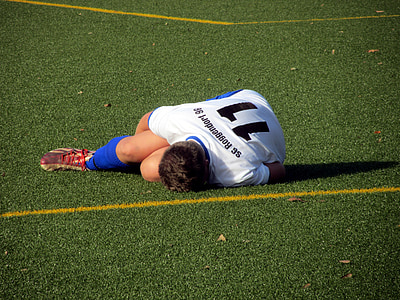 man wearing white and black soccer uniform lying on green grass field thumbnail