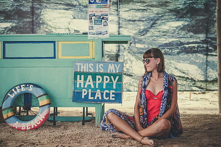 woman wears multicolored shirt sitting beside this is my happy place signage during daytime thumbnail