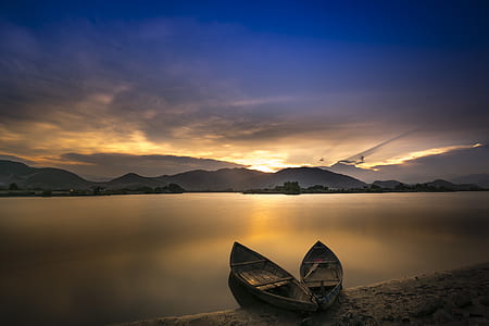 two boats on seashore across mountain during golden hour thumbnail