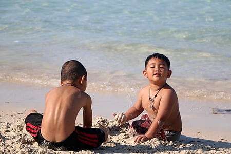 two boys playing sand near body of water thumbnail