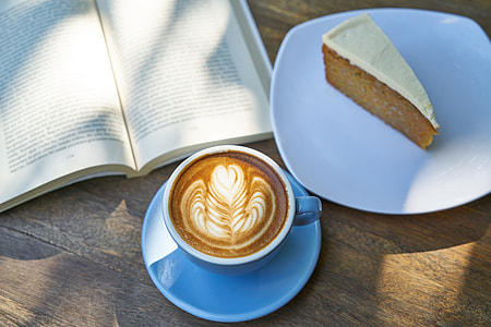 latte with flower froth art beside plate with slice of cake thumbnail