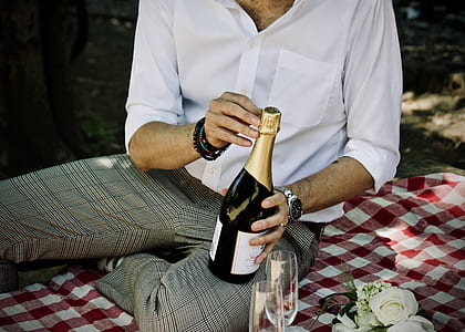 person opening wine bottle while sitting on red and white textile outdoor during daytime thumbnail