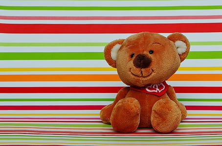 brown bear plush toy sitting on multicolored striped panel thumbnail