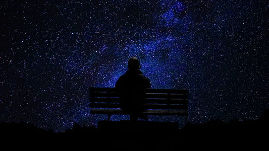 silhouette photo of person sitting on bench and looking sky with stars thumbnail