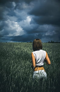 woman in white crop top and jeans walking in grassland under cloudy skies thumbnail