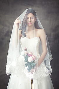 Woman in White Strapless Sweetheart Wedding Dress With Rose Bouquet Covered in White Veil thumbnail