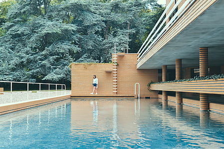 woman walking beside swimming pool near green leafed trees during daytime thumbnail