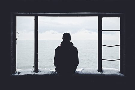 man sitting on window panel watching ocean view during daytime thumbnail