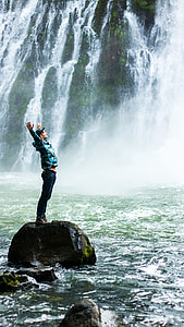 man standing on rock near waterfall thumbnail