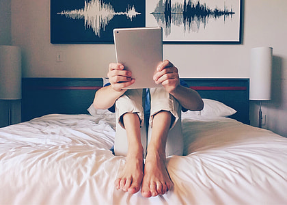 photo of person holding gray tablet while sitting on bed thumbnail
