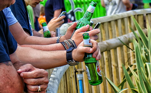 four men leaning on brown bamboo balustrade holding green bottles thumbnail