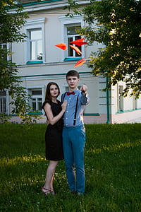 man and woman standing on grassland throwing orange paper planes thumbnail