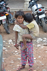 child carrying toddler while standing near parked motorcycles during daytime thumbnail