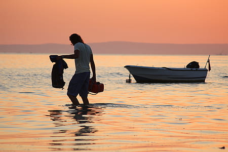 man standing in water near white boat thumbnail