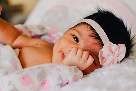 baby wearing headband lying on white covered bed thumbnail