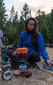 woman squatting on ground beside camp gas stove thumbnail