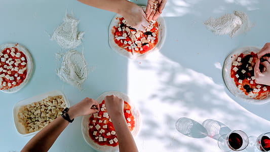 three person pouring cheeses on pizza doughs during daytime thumbnail