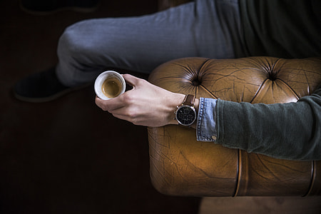 person sitting on brown leather couch holding coffee cup thumbnail