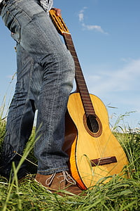 person wearing blue denim jeans carrying guitar on green grass thumbnail