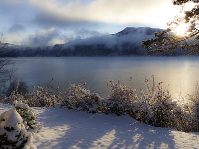 snow covered ground and trees by the river overlooking mountain and sunrise under blue and white cloudy sky thumbnail
